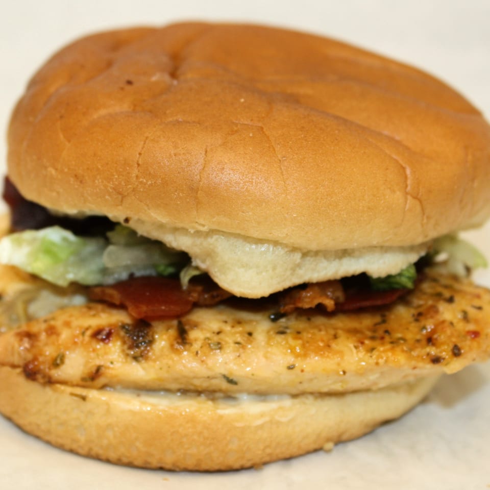 Joe's To Go grilled chicken sandwich with bacon, lettuce, and mayonnaise on a bun.