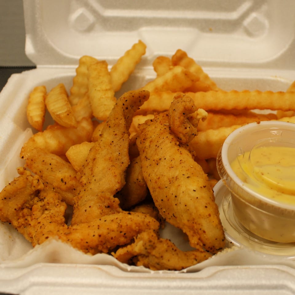 Crispy chicken tenders and crinkle-cut fries with a side of dipping sauce in a styrofoam container.