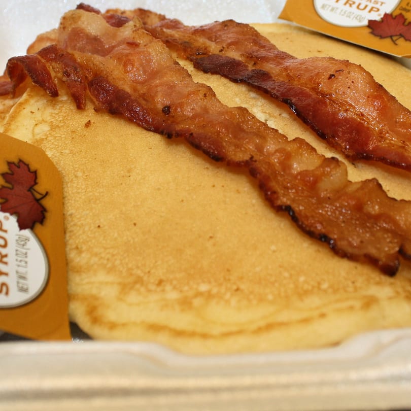 Golden pancakes topped with crispy bacon strips and a syrup packet from Joe's To Go.