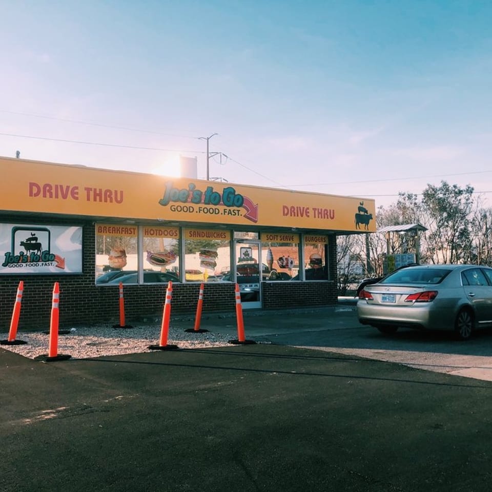 Joe's To Go drive-thru restaurant with a silver car, orange cones, and blue sky.