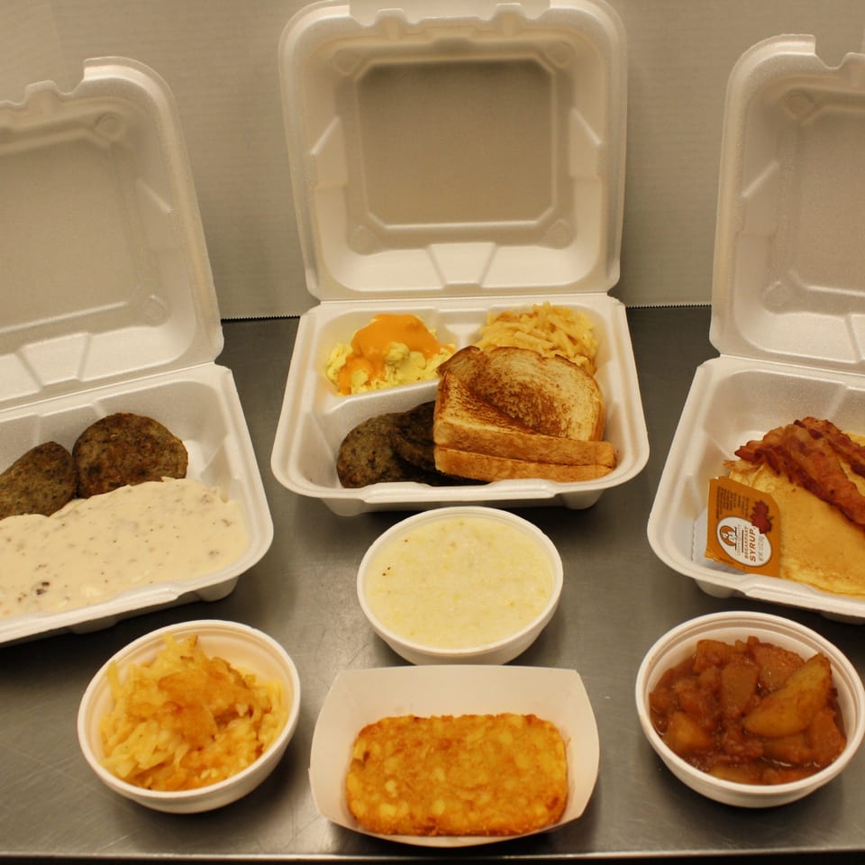 Three Joe's To Go breakfast meals in takeout containers with sides of hash browns, grits, and apples.